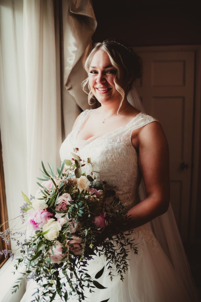 A bride holding her flowers next to the window at hatherley manor