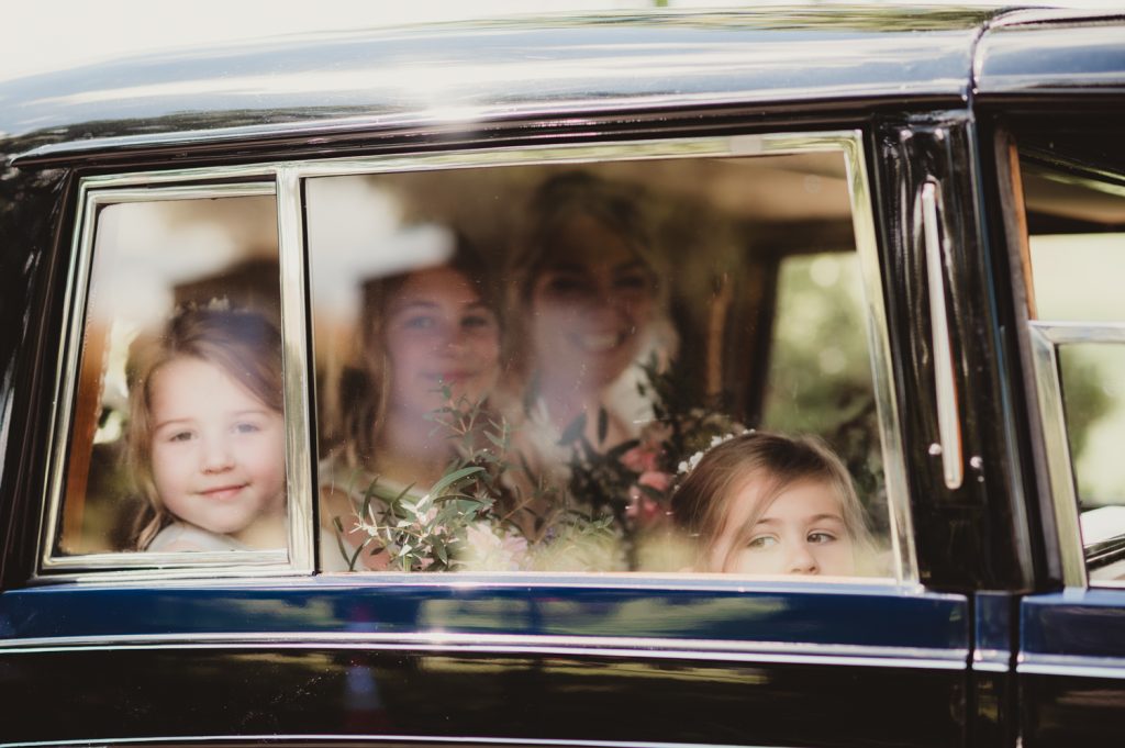 a bride and flowergirls through the car window arriving at Boddington Church