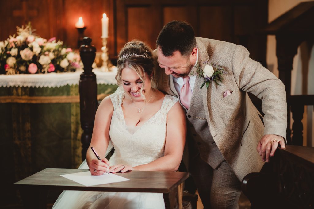 Bride and groom smiling as they sign the marriage certificate at Boddington church,