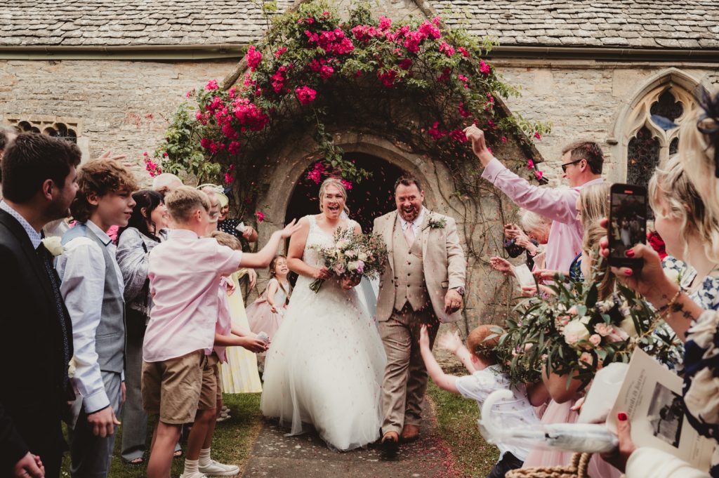 A bride and groom as they exit Boddington Church having confetti thrown over them