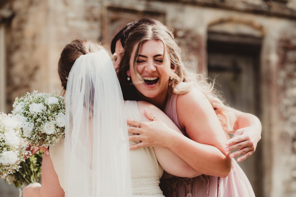 A bride hugging and laughing with her bridesmaids after she has got married in the Cotswolds