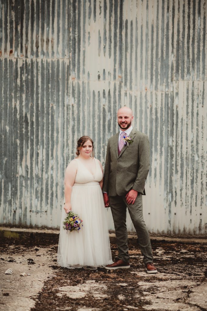 A bride and groom in front of a farm barn in the cotswolds