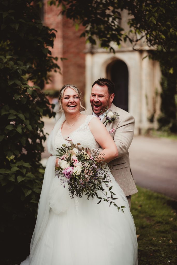 A bride and Groom laughing for photos outside Hatherley Manor Hotel in Cheltenham