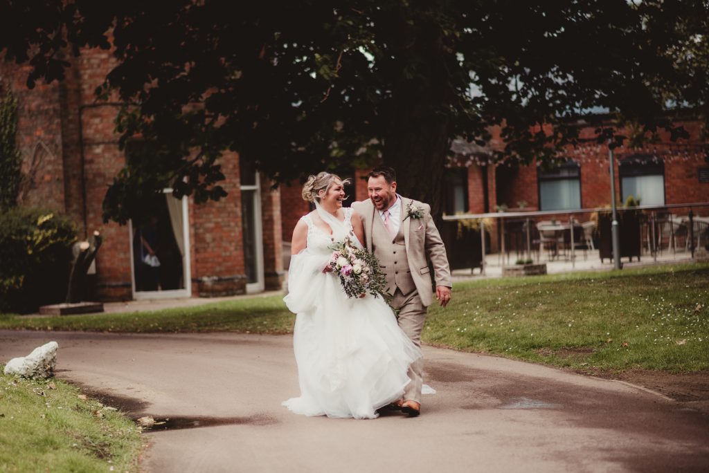 Bride and groom walking arm in arm, smiling and laughing at Hatherley Manor Hotel and Spa