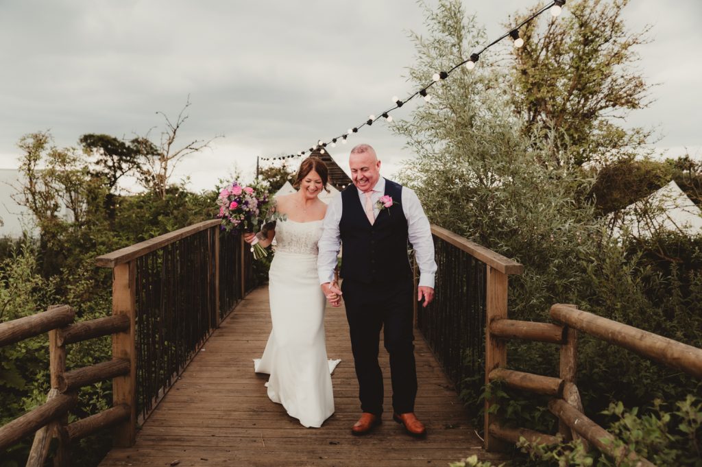 bride and groom walking accross the bridge at Hardwick Moat wedding