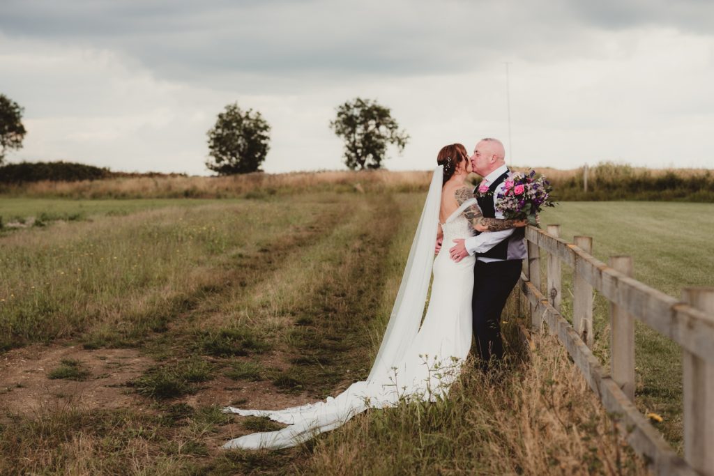 Bride and groom kissing against fence at Hardwick Moat Weddings