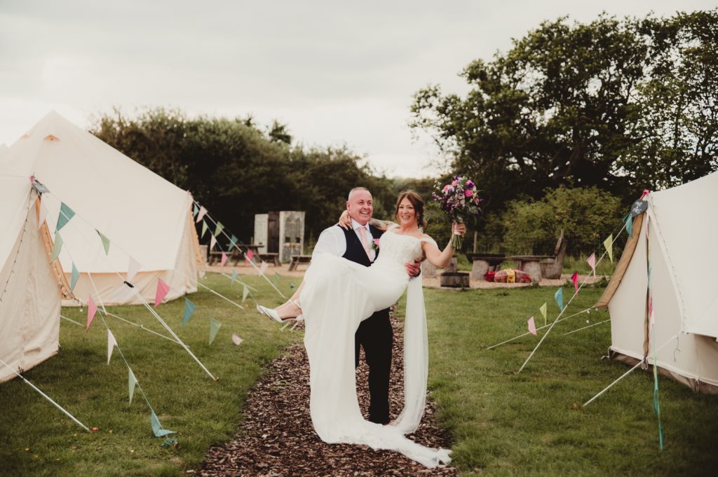 Groom lifting bride up amongst the glamping area of hardwick moat weddings