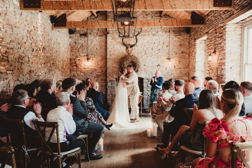 Bride and grooms first kiss during their rustic ceremony at White Horse Barn in Bristol